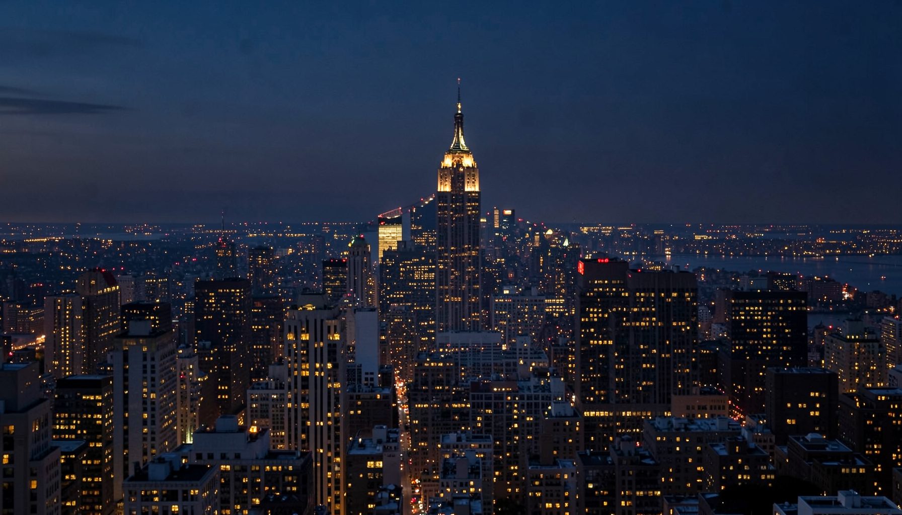 A wide-angle view of a New York City skyline at dusk, with deep navy and charcoal tones blending into warm amber lights across the skyline, conveying ambition and possibility.